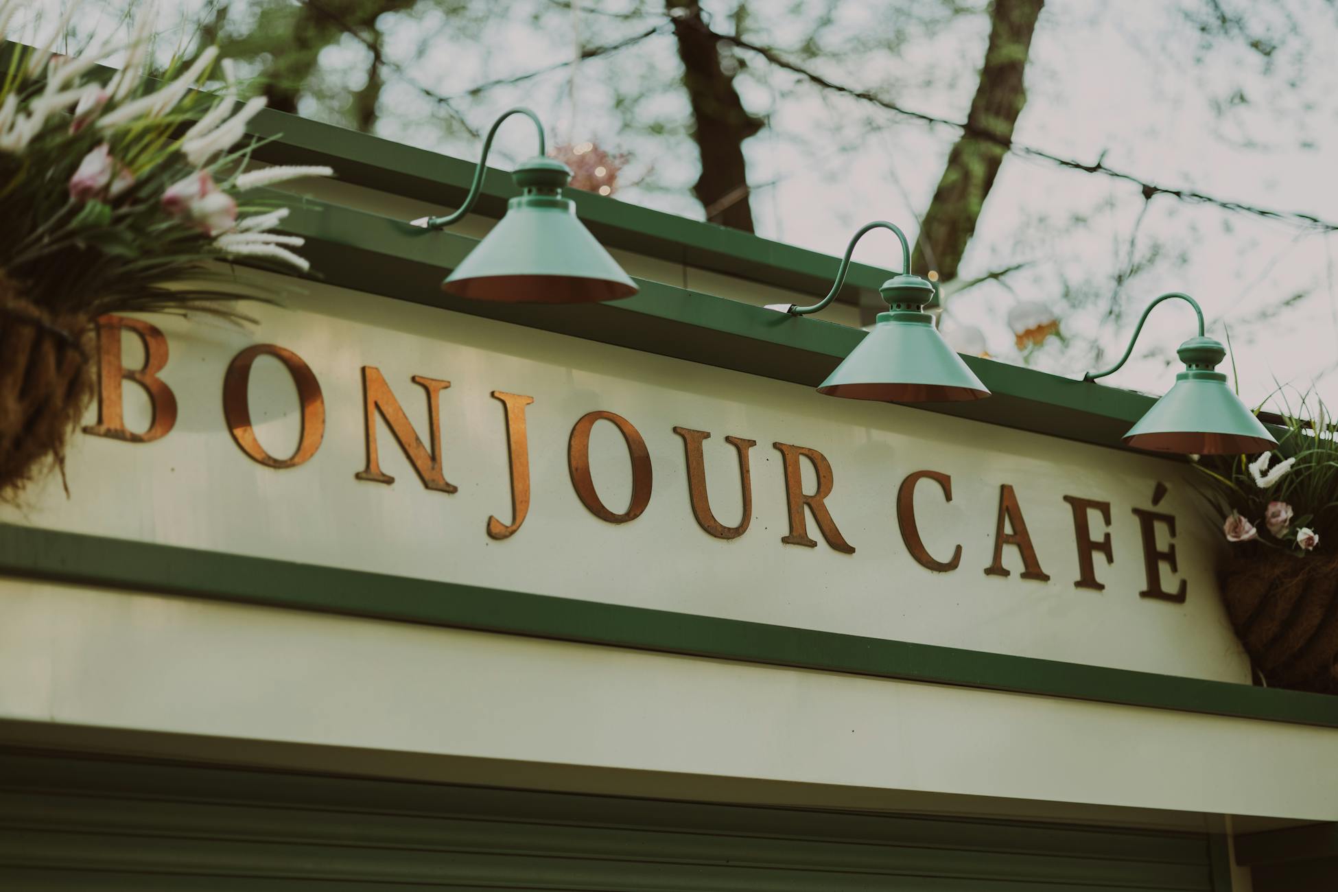 Outdoor shot of Bonjour Café sign with vintage lamps and flowers.