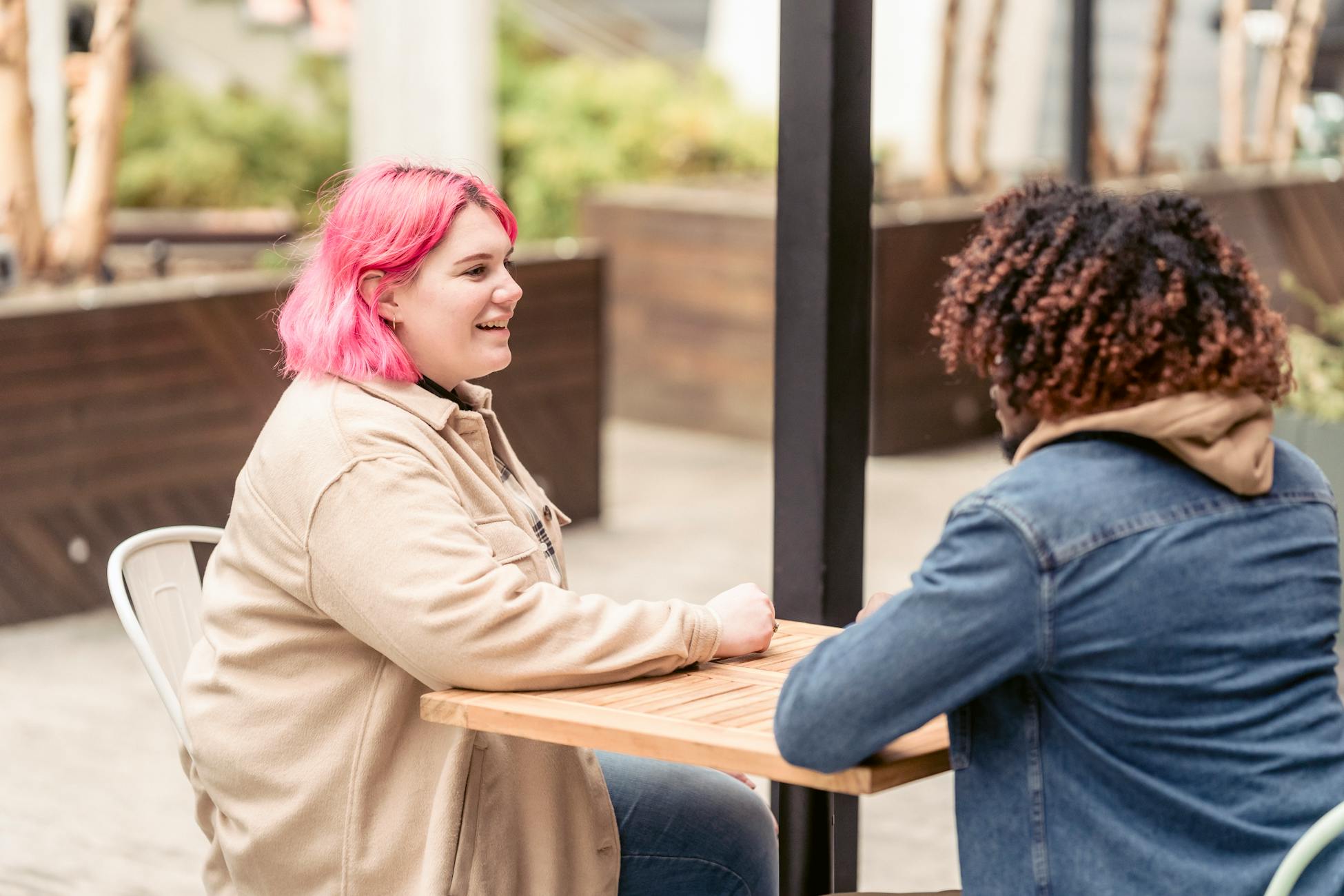 Two adults with colorful hair enjoying a casual chat at an outdoor cafe.