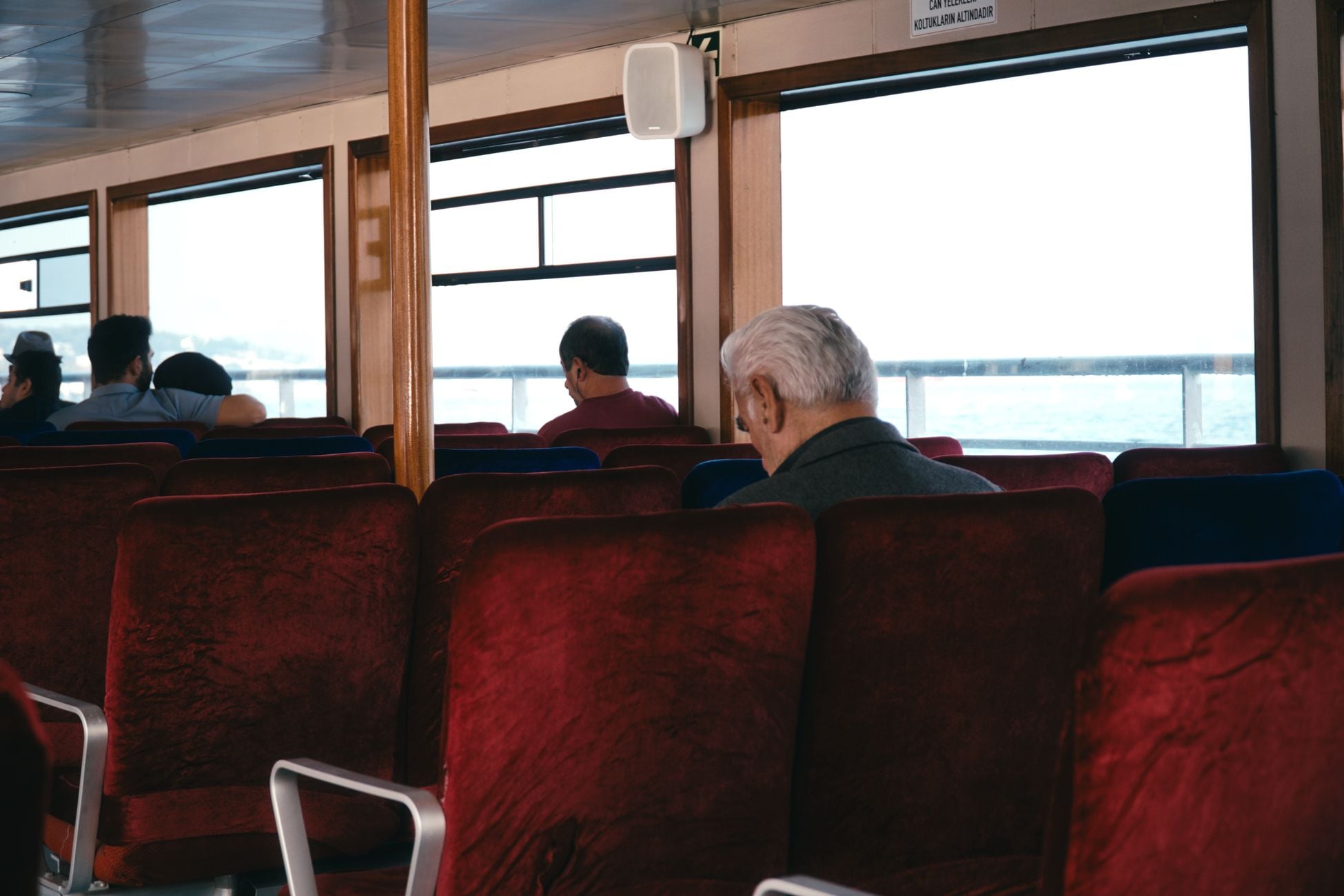Passengers relax on a ferry with red seats, enjoying a serene view outside. Travel and relaxation theme.