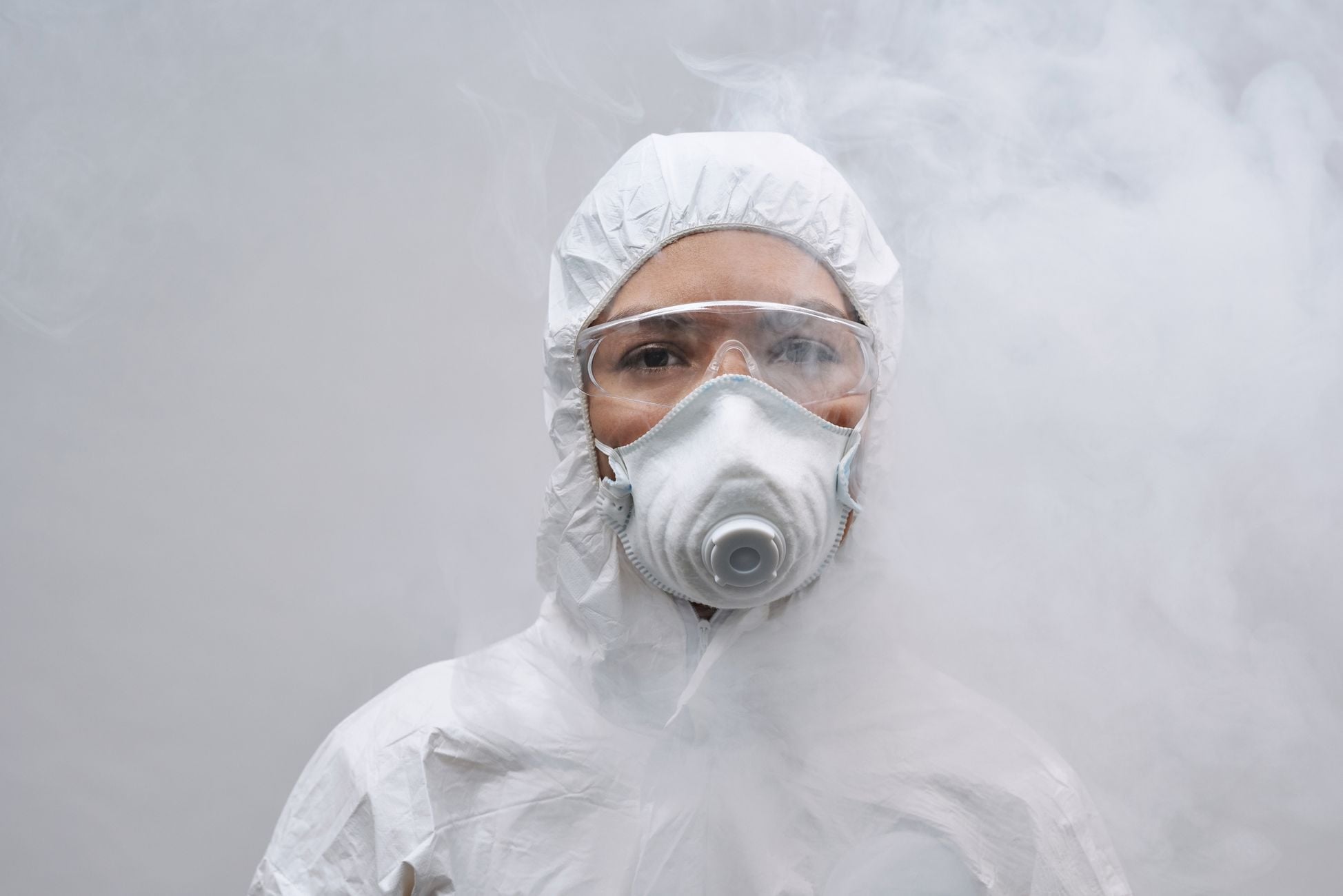 Close-up of person wearing protective suit, mask, and goggles amidst smoke.