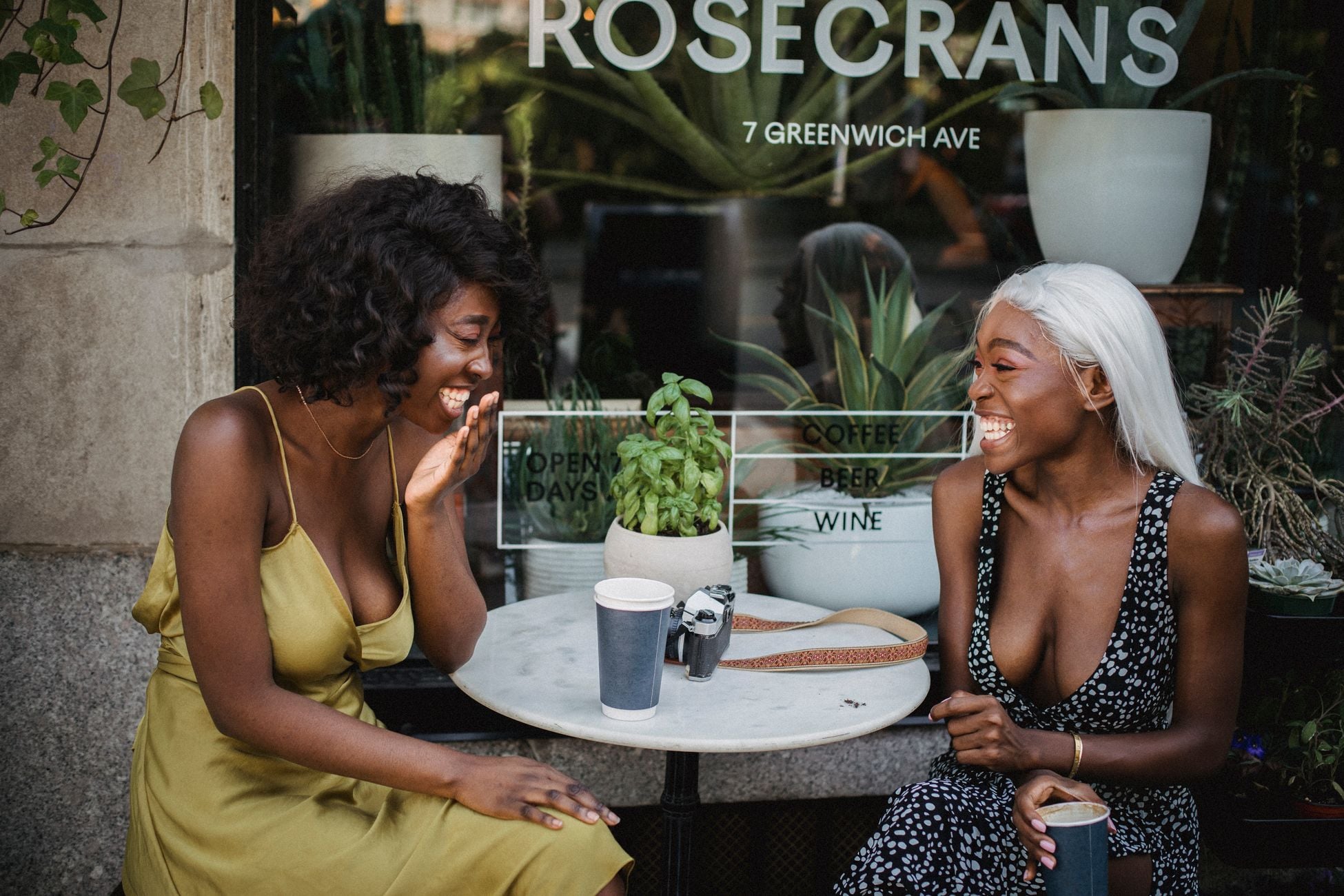 Two friends share laughter over coffee at a café, creating a joyful outdoor scene.