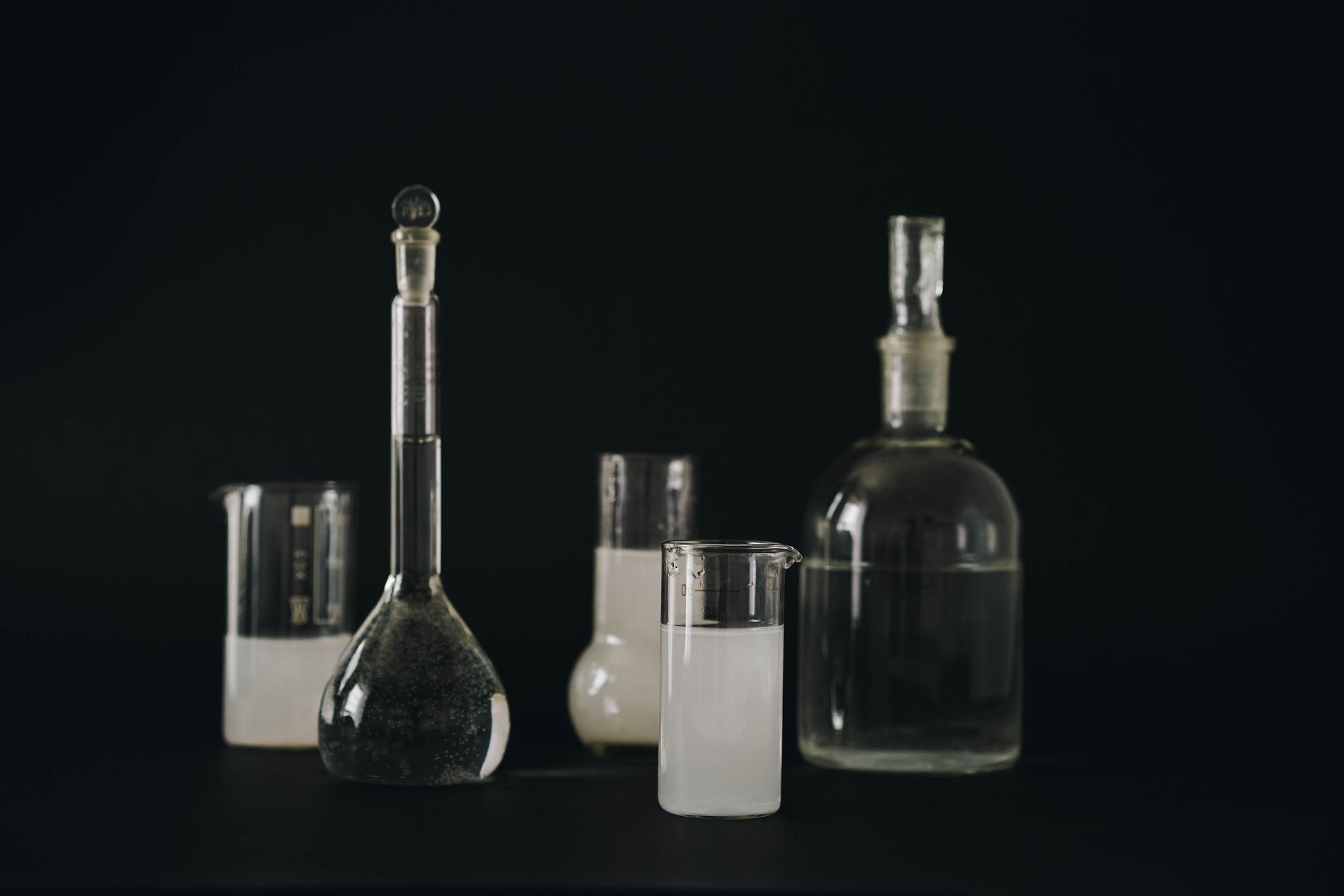 Close-up of various laboratory glassware filled with liquids on a dark background.