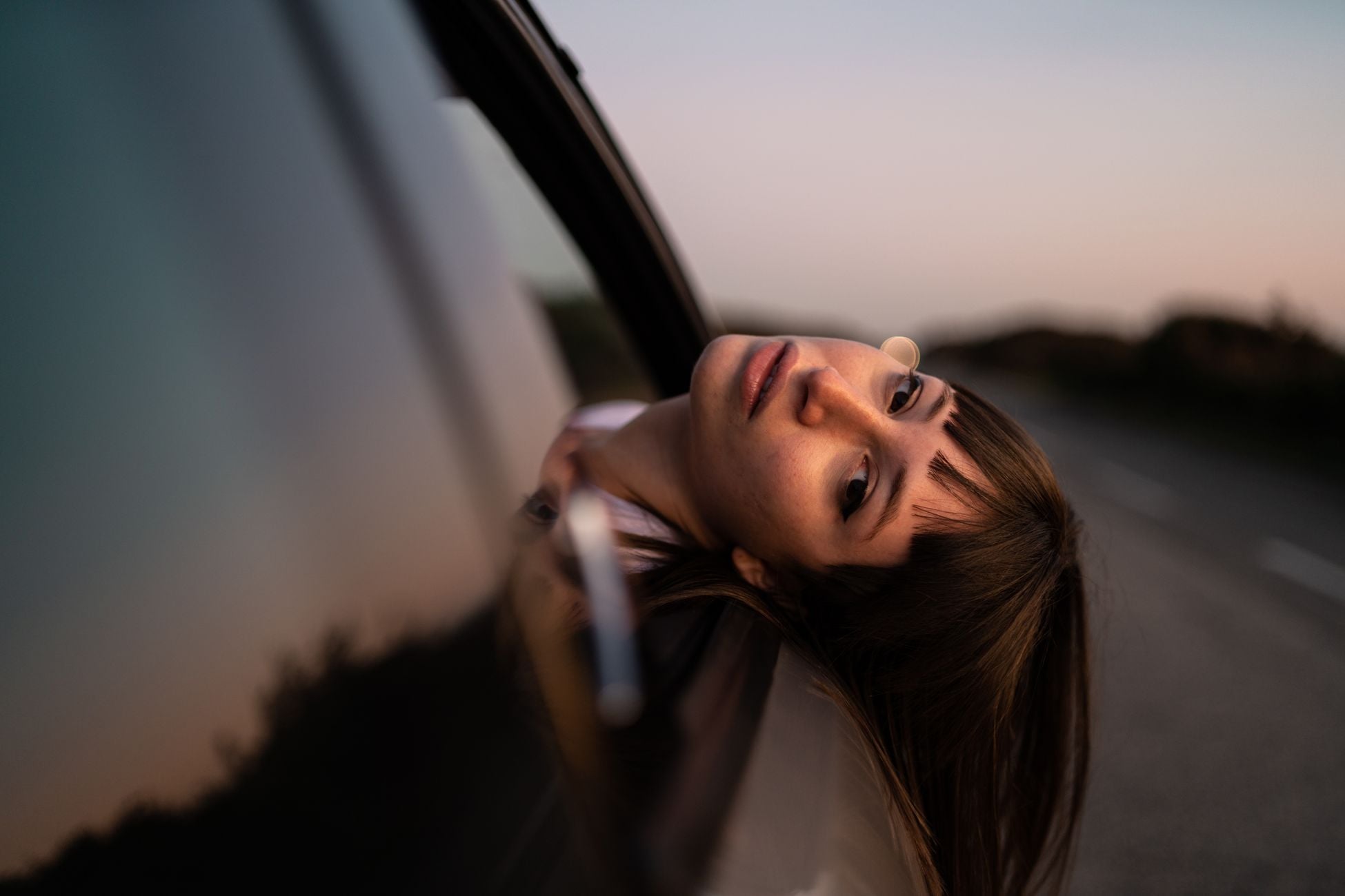 A serene woman leans out a car window, gazing thoughtfully. Capturing a moment of reflection at dusk.