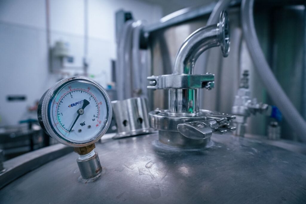 Close-up of a pressure gauge on a stainless steel tank in a sterile industrial setting, showcasing manufacturing technology.